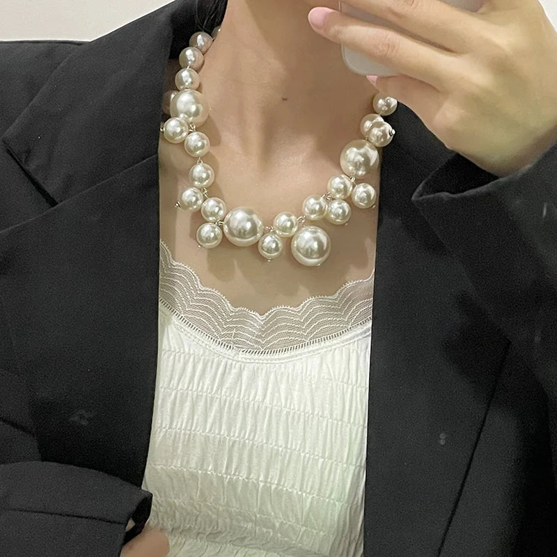 A close-up of an elegant simulated pearl choker necklace worn by a person, displayed against a white top and black blazer.