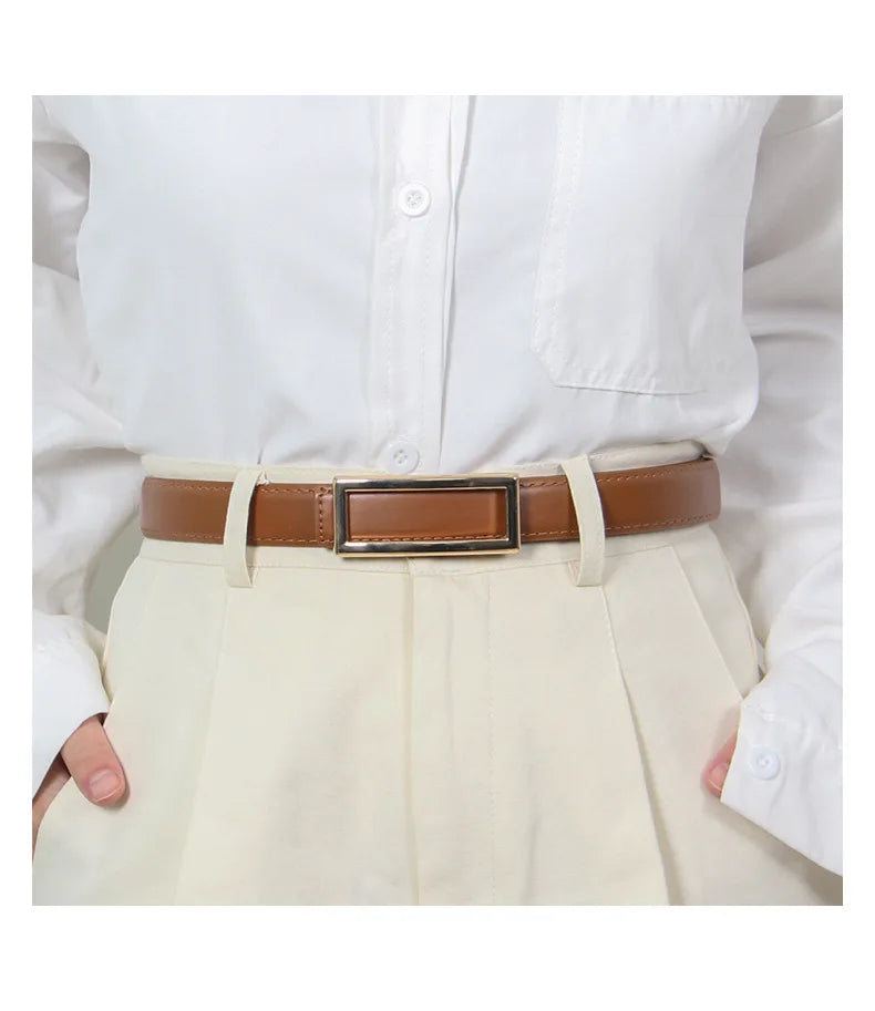 A close-up of a tan faux leather belt worn over a cream-colored skirt and white shirt.
