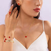A close-up shot of a woman wearing a gold necklace and bracelet set featuring red enamel plum blossom charms.