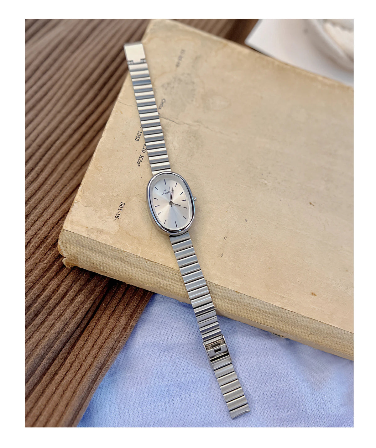 Une montre en quartz argentée avec un bracelet métallique repose sur un vieux livre.