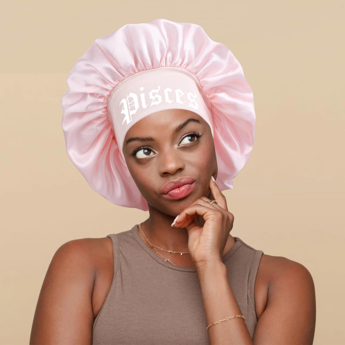 A woman wearing a pink satin sleep bonnet with a white Pisces wrap band.