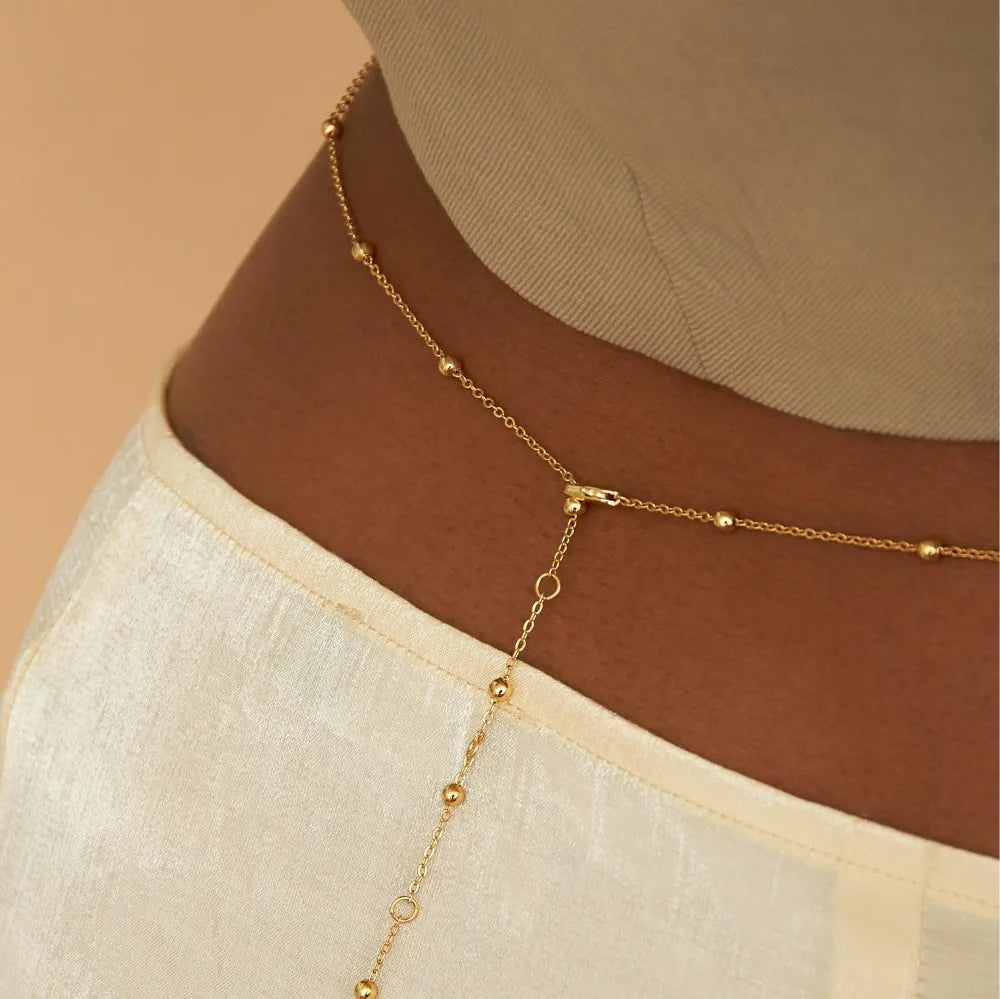 A close-up of a delicate gold belly chain body jewelry necklace worn on a neck.