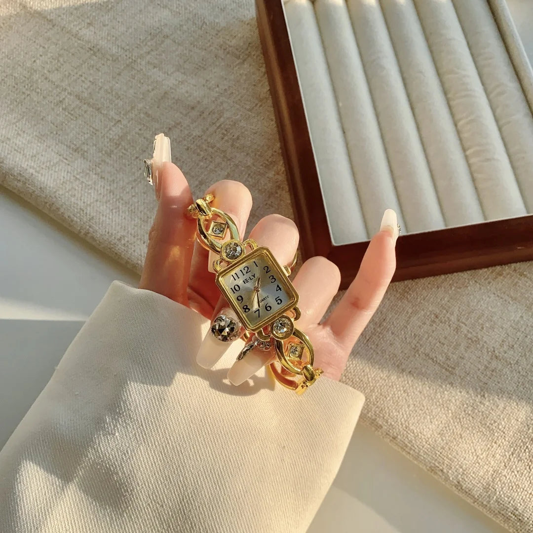 A hand holds an elegant gold quartz fashion wristwatch against a light beige fabric and a wooden frame.