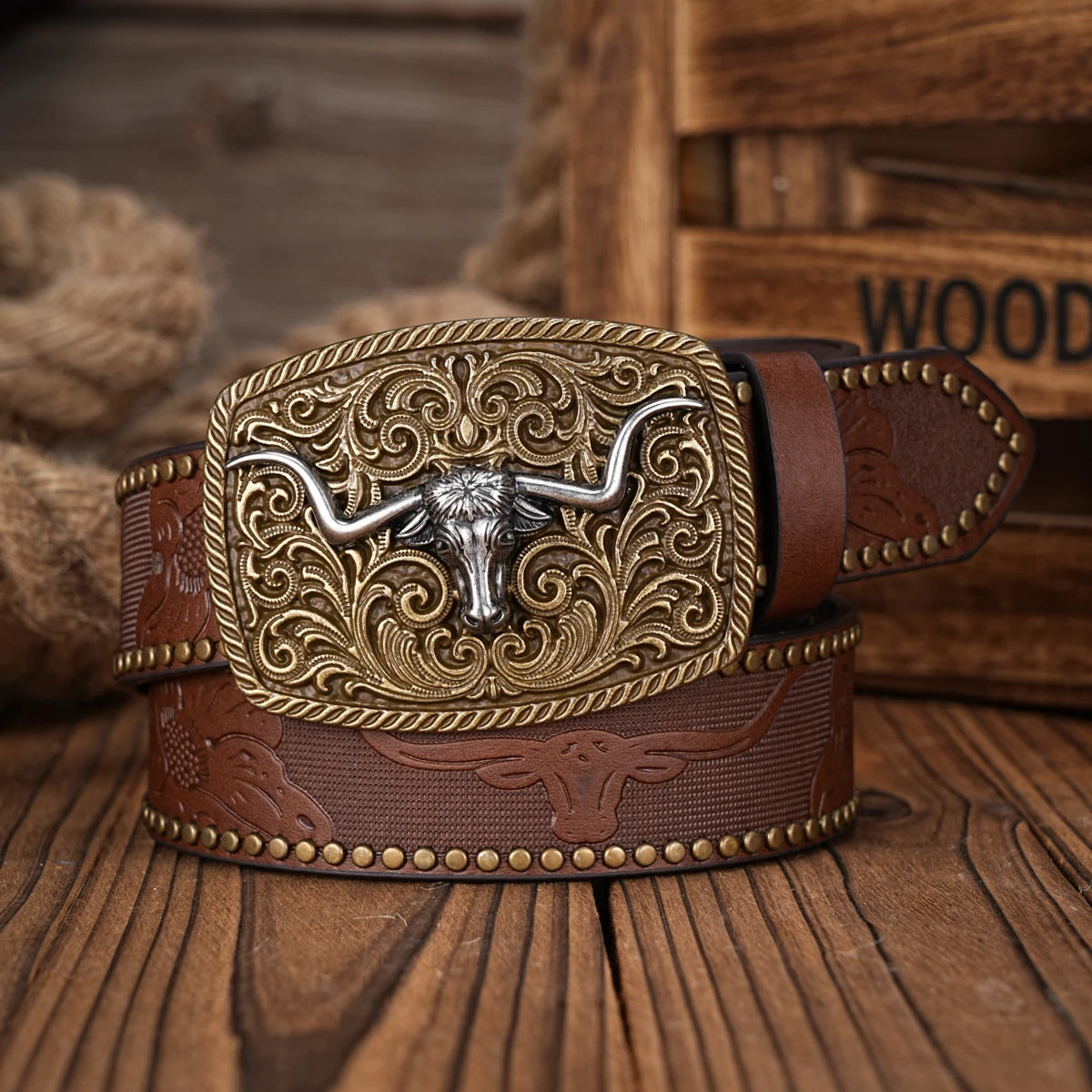 A brown PU leather belt with a silver floral engraved buckle resting on a wooden surface.