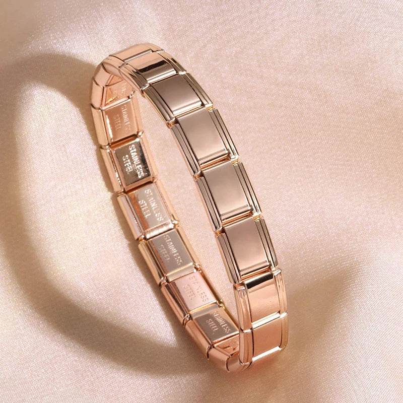 A close-up shot of a rose gold stainless steel charm bracelet displayed on a soft pink fabric.