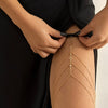 A woman is wearing a delicate gold crystal body chain jewelry on her thigh.
