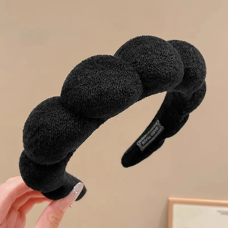 A black cloud sponge hair accessory headband is being held by a hand.
