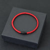 A red thread charm bracelet is displayed on a dark gray box.
