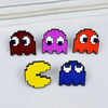 A set of four enamel pins featuring characters inspired by Pac-Man, including red, purple, orange, and blue designs.