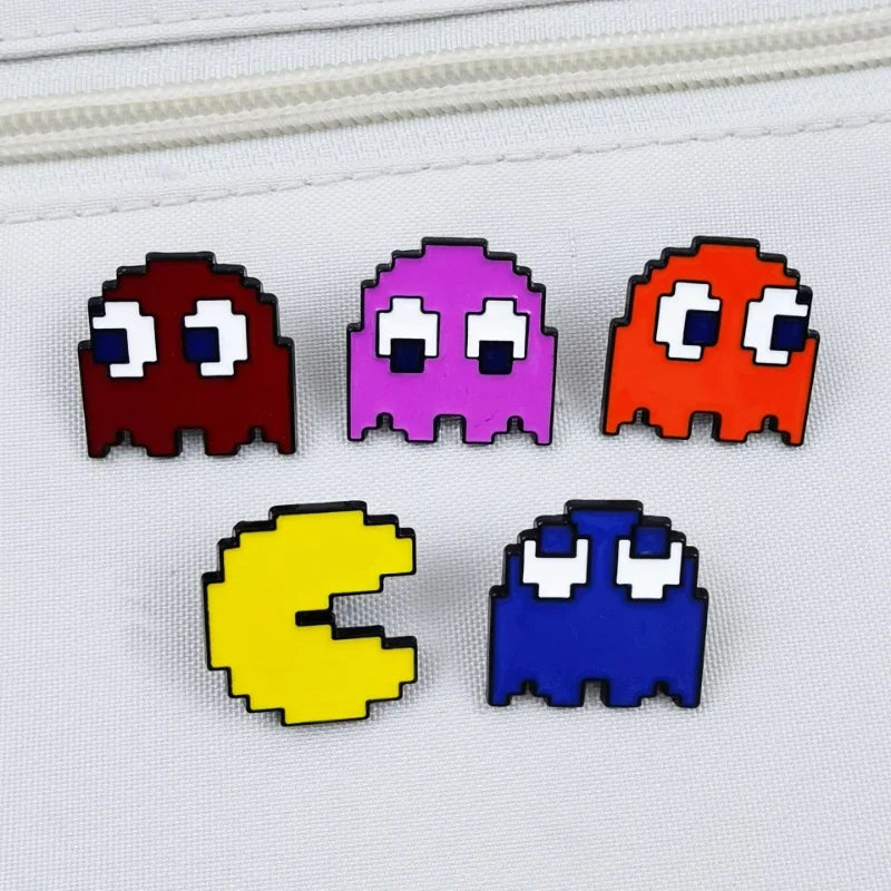 A set of four enamel pins featuring characters inspired by Pac-Man, including red, purple, orange, and blue designs.