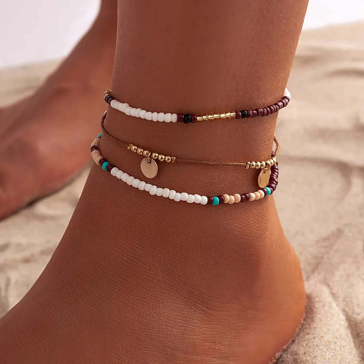 A set of bohemian sequin rice bead anklets worn on a person's ankle.
