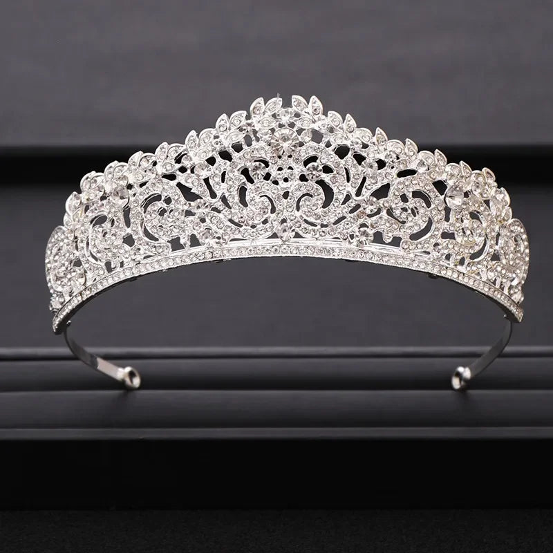 A sparkling silver crystal bridal crown with intricate floral detailing displayed on a dark surface.