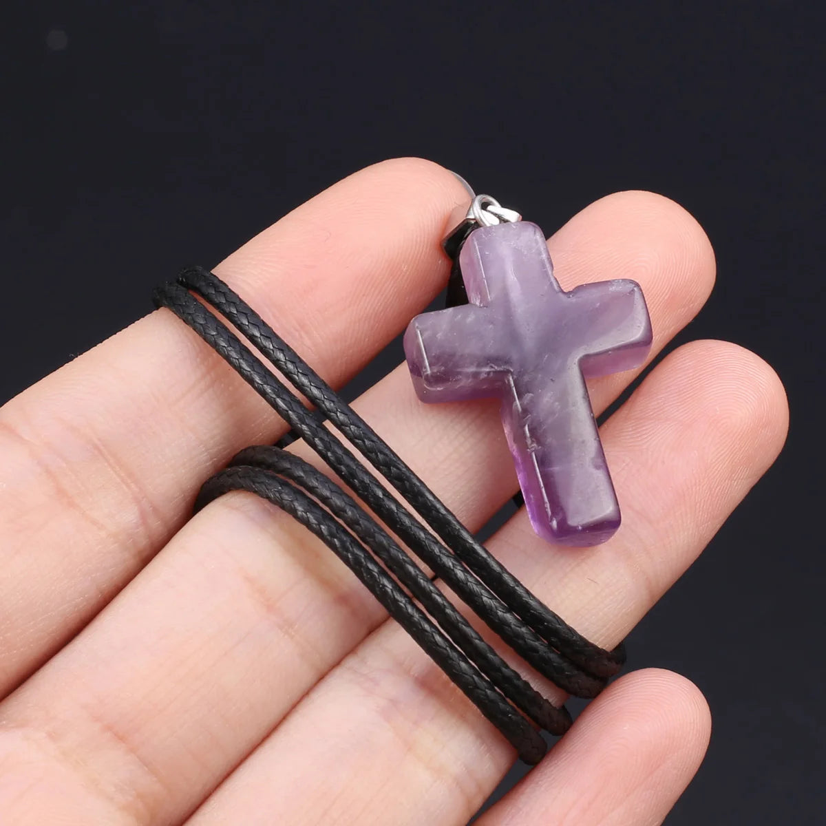 Eine Hand hält eine lila Tigerauge-Agat-Kreuz-Anhänger-Kette mit schwarzem Band.