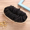 A bundle of black boho seamless elastic hair ties resting on a light beige oval dish.