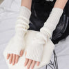 A pair of white knitted fingerless gloves being held by a person against a white background.