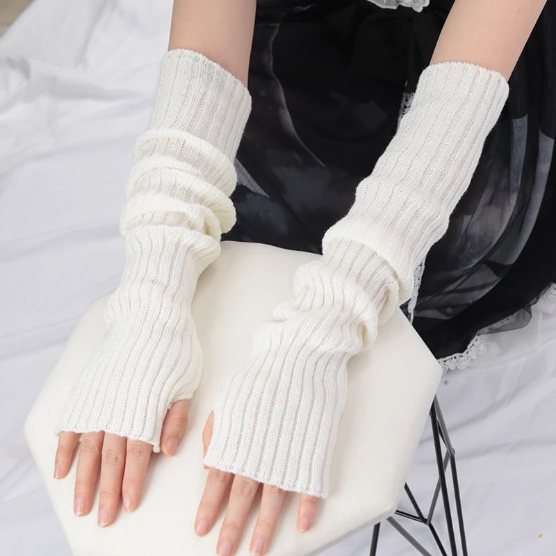 A pair of white knitted fingerless gloves being held by a person against a white background.