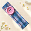 A pink button headband with a plaid fabric tie and white daisy flowers.