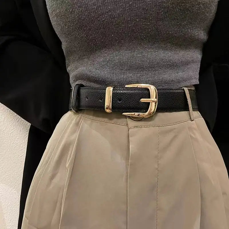 Nahaufnahme eines eleganten goldenen Kunstledergürtels mit Schnalle über einem grauen Pullover und einem beigen plissierten R