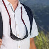 A person wearing a white shirt with a black and red lanyard holding a pair of sunglasses.