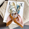 A light pink silk scarf with blue floral patterns and gold trim is displayed on a white card.
