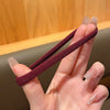 A hand holds a dark maroon elastic hair tie against a blurred wooden background.
