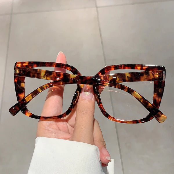 A hand holds a pair of brown tortoiseshell square eyeglasses frames against a light gray background.