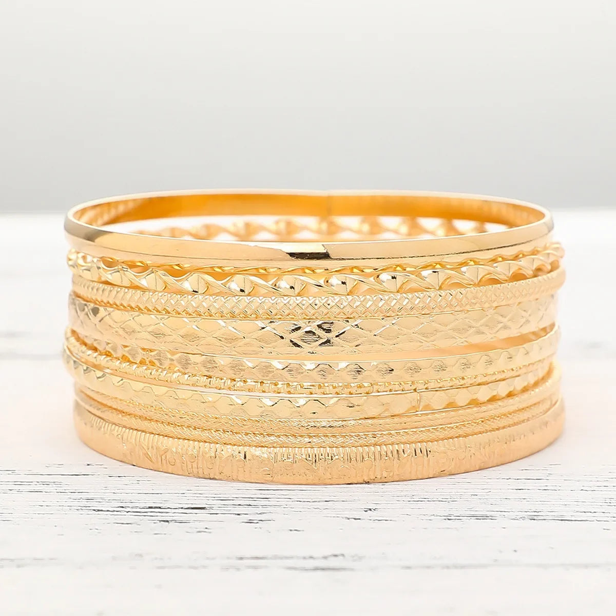A stack of elegant gold hexagon star twist bangles displayed on a white surface.