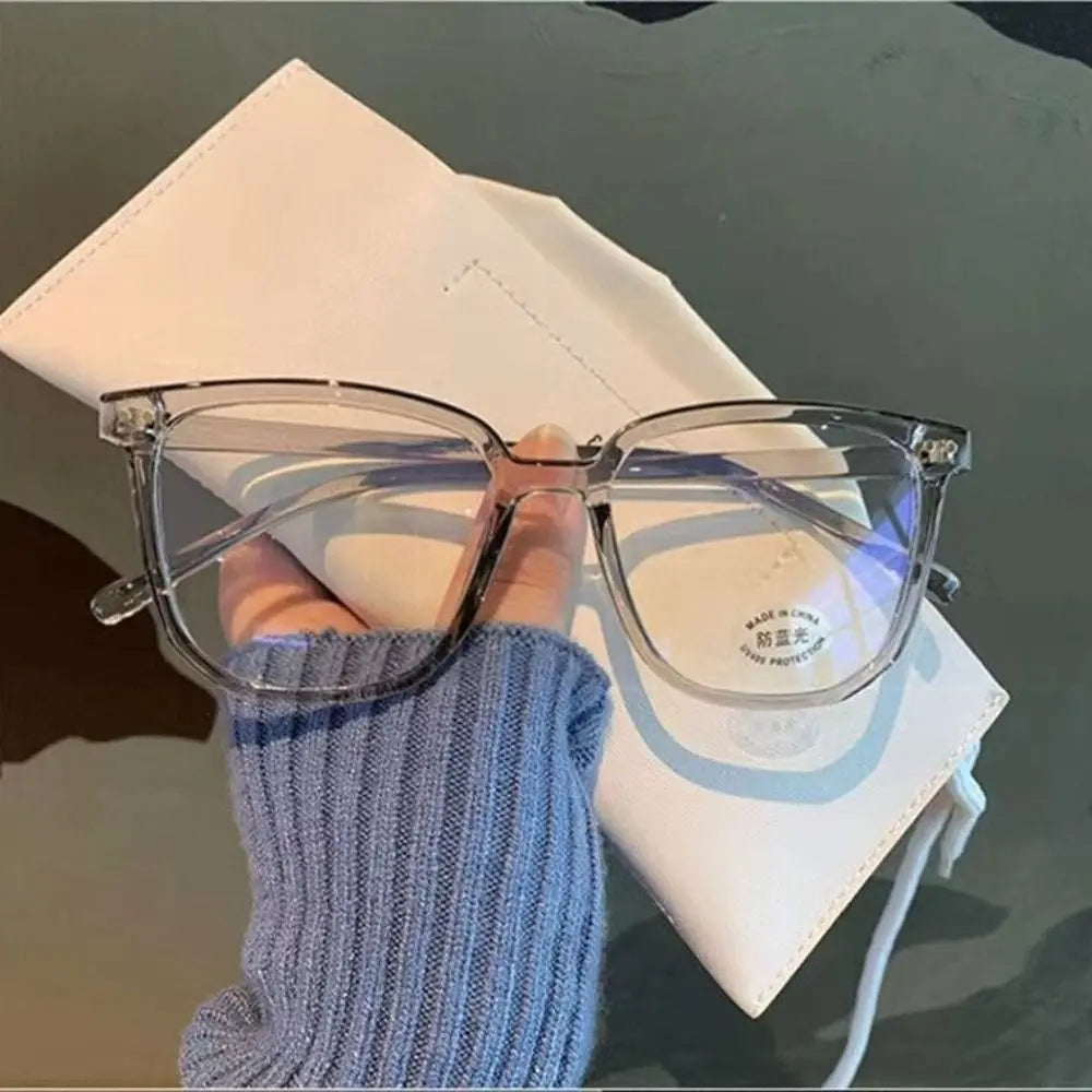 A pair of clear-framed anti-blue light spectacles resting on a white notebook next to a blue knitted sleeve.