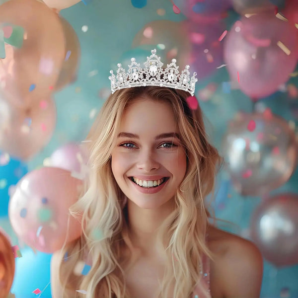 A smiling blonde woman wearing a sparkling rhinestone tiara headband surrounded by pink and blue confetti balloons.