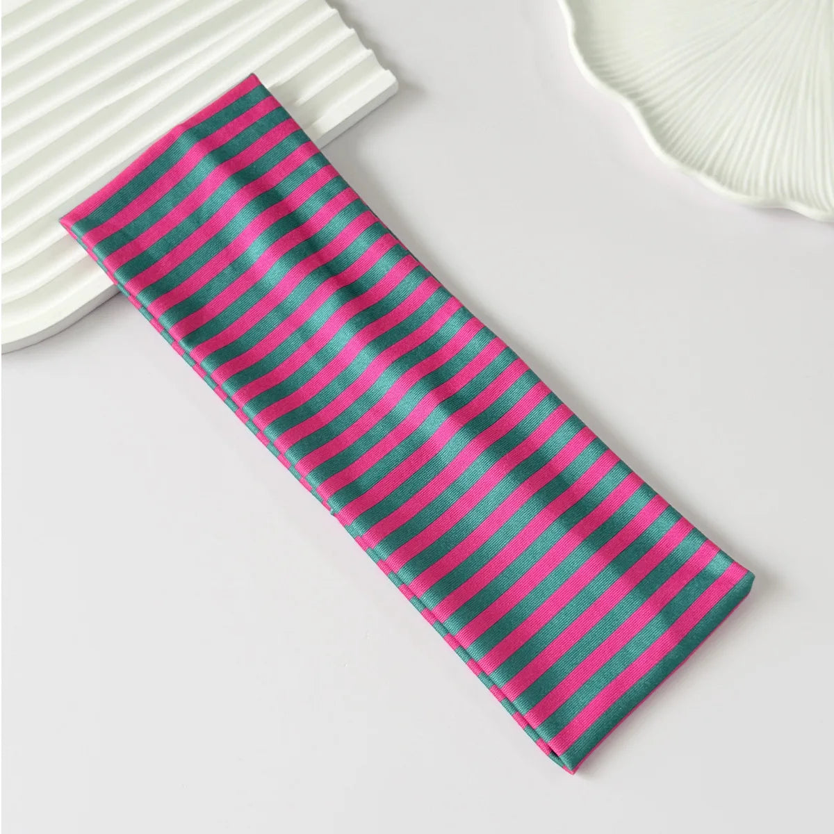 Gros plan d'un élastique pour cheveux rayé rose et vert sur une surface blanche.
