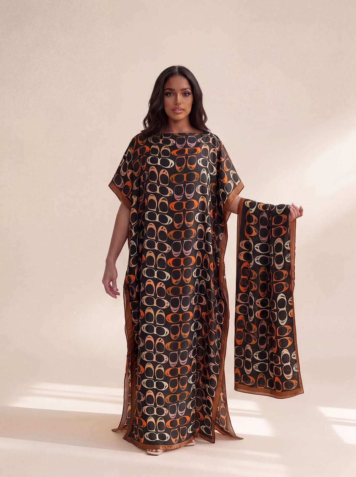 A woman models an elegant long silk blend cover-up robe dress featuring a dark brown and orange patterned fabric.