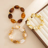 Un set de trois bracelets charm vintage en résine acrylique bohème avec des pierres d'ambre, or et blanc.