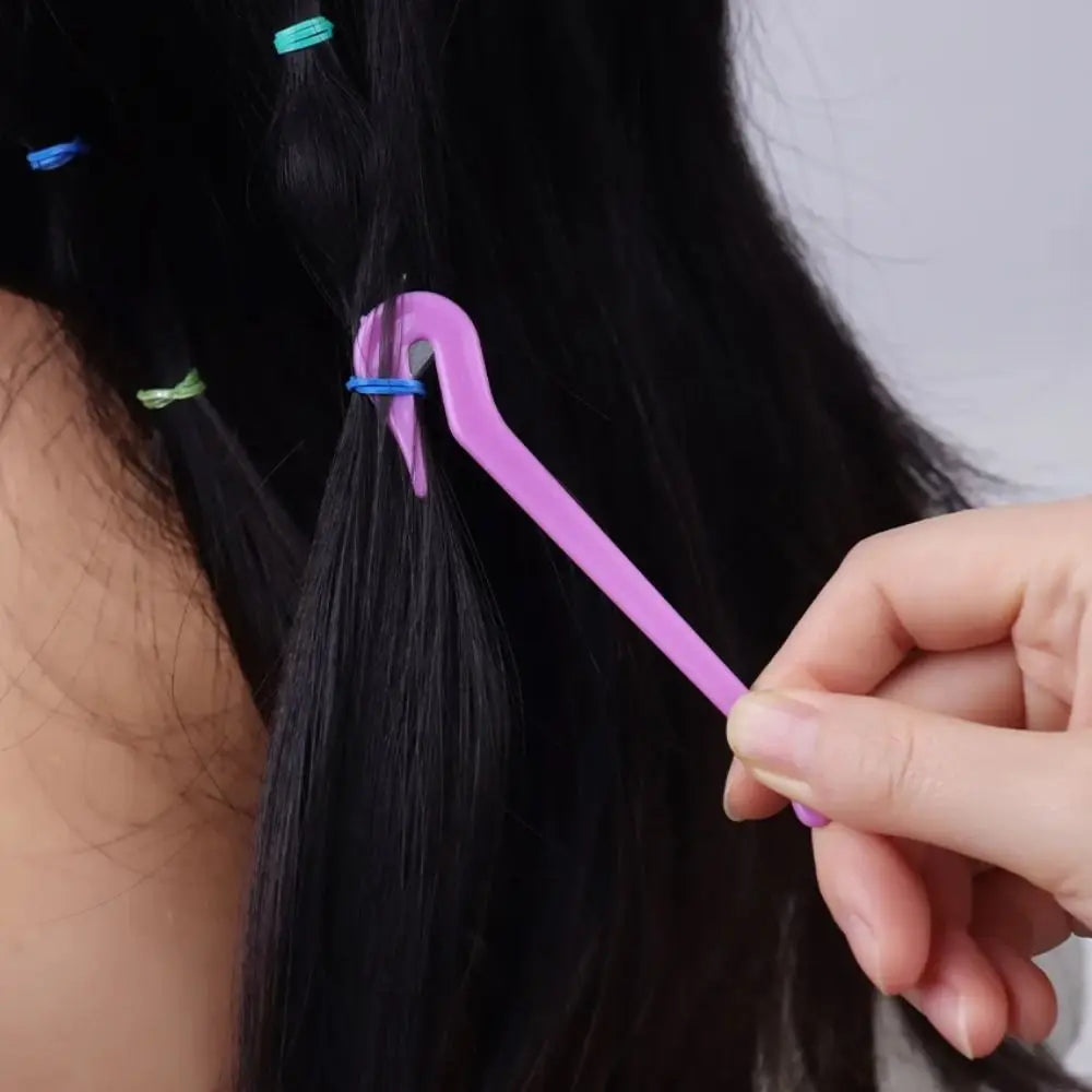 A hand holds a purple hair tool used for removing elastic and rubber bands from black hair.