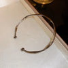A minimalist gold-tone twisted cuff bangle displayed in a light-colored box.