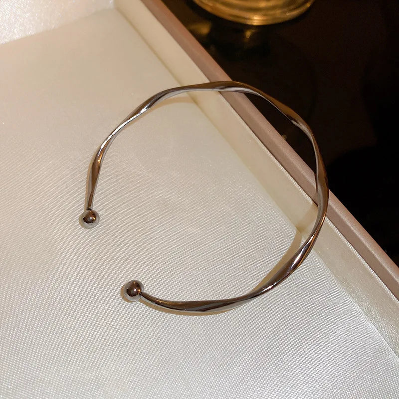 A minimalist gold-tone twisted cuff bangle displayed in a light-colored box.