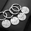 A set of silver stainless steel keychains with engraved names and drawings, displayed on a dark surface.