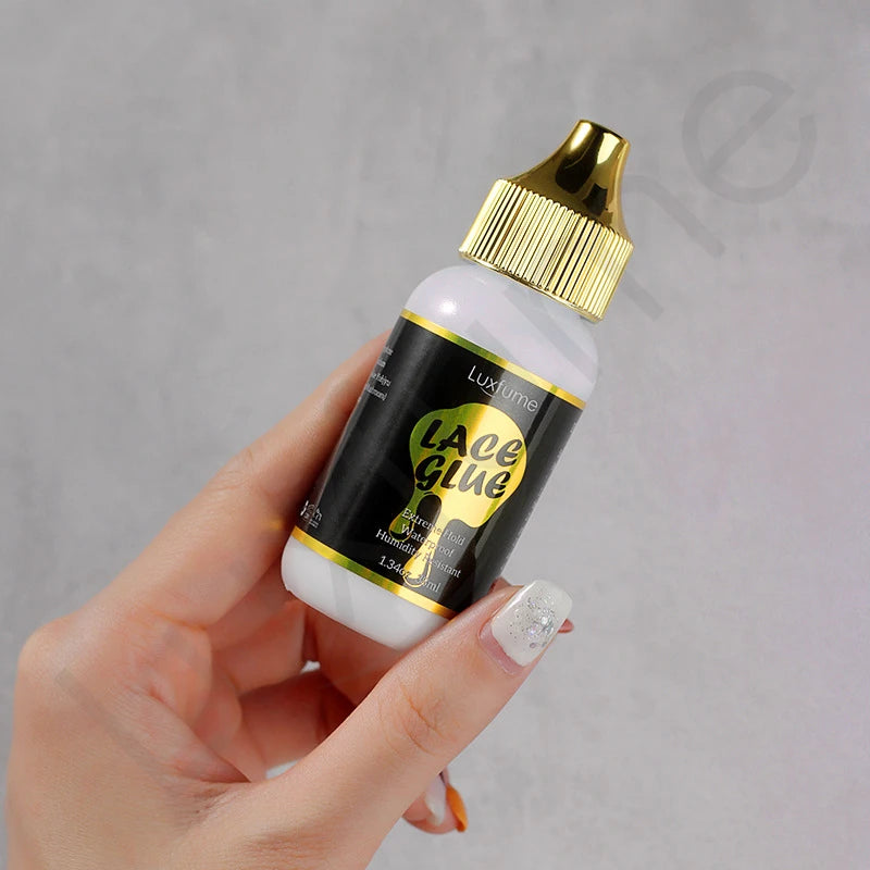 Eine Hand hält eine Flasche LuxeLume Lace Glue, eine klare Flüssigkeit in einer schwarzen Flasche mit goldener Kappe.