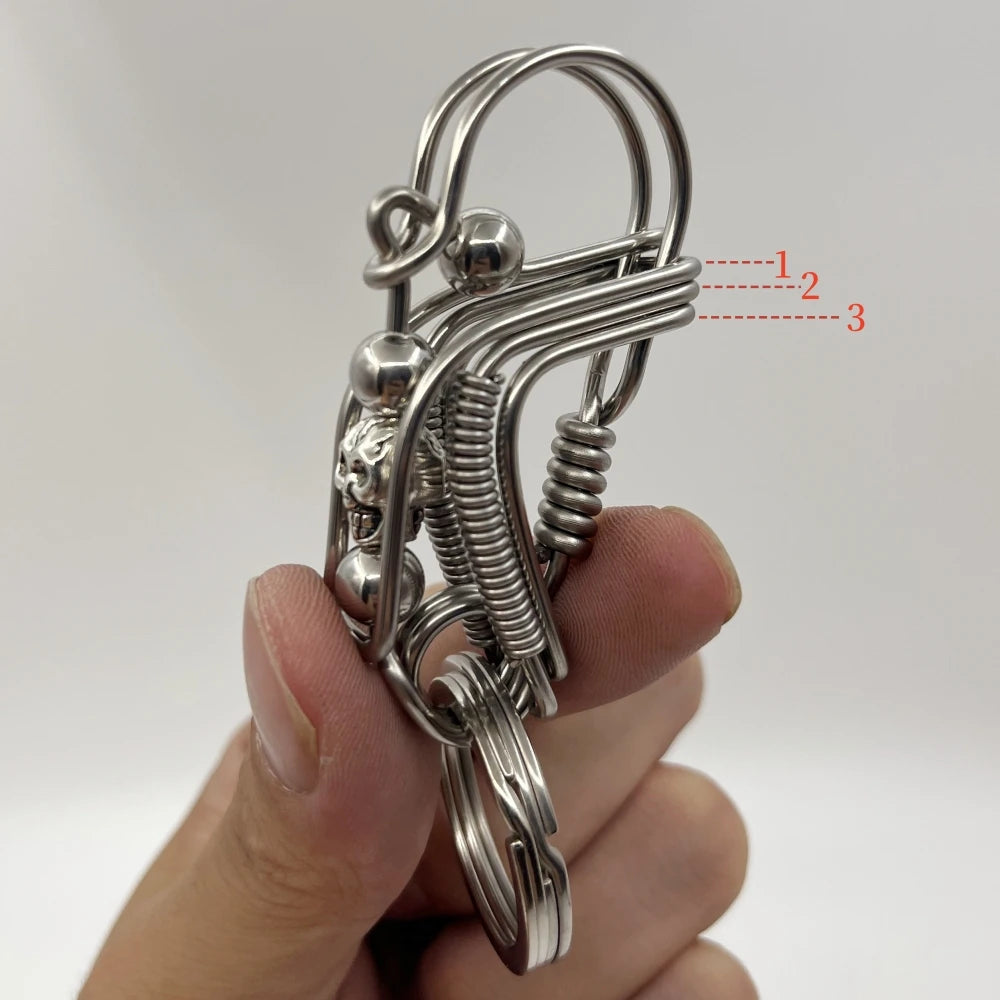Un porte-clés mécanique en acier inoxydable avec une boucle et un ressort enroulé est tenu dans une main.