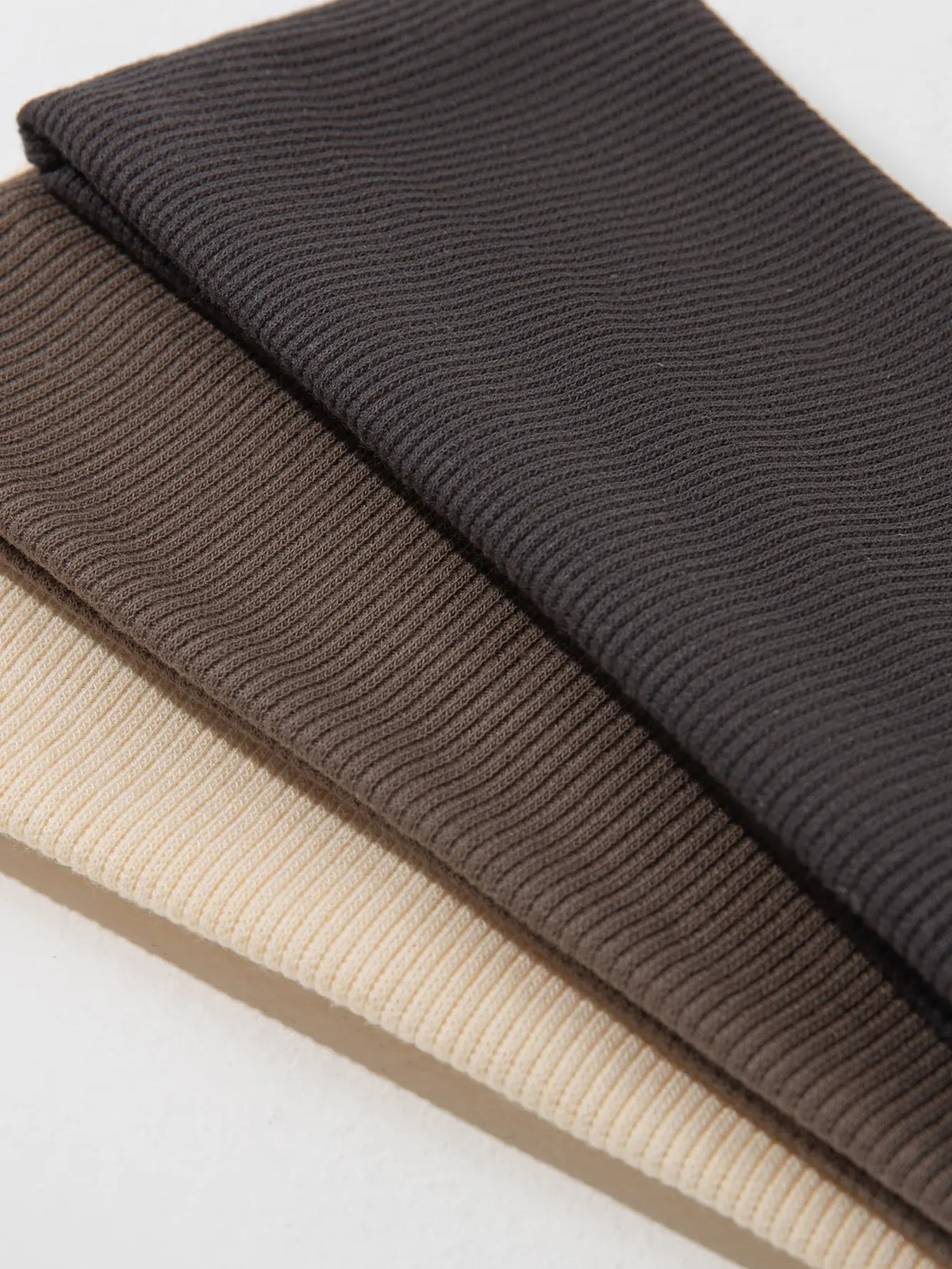 Three solid color fashion headbands stacked diagonally in shades of dark gray, brown, and beige.