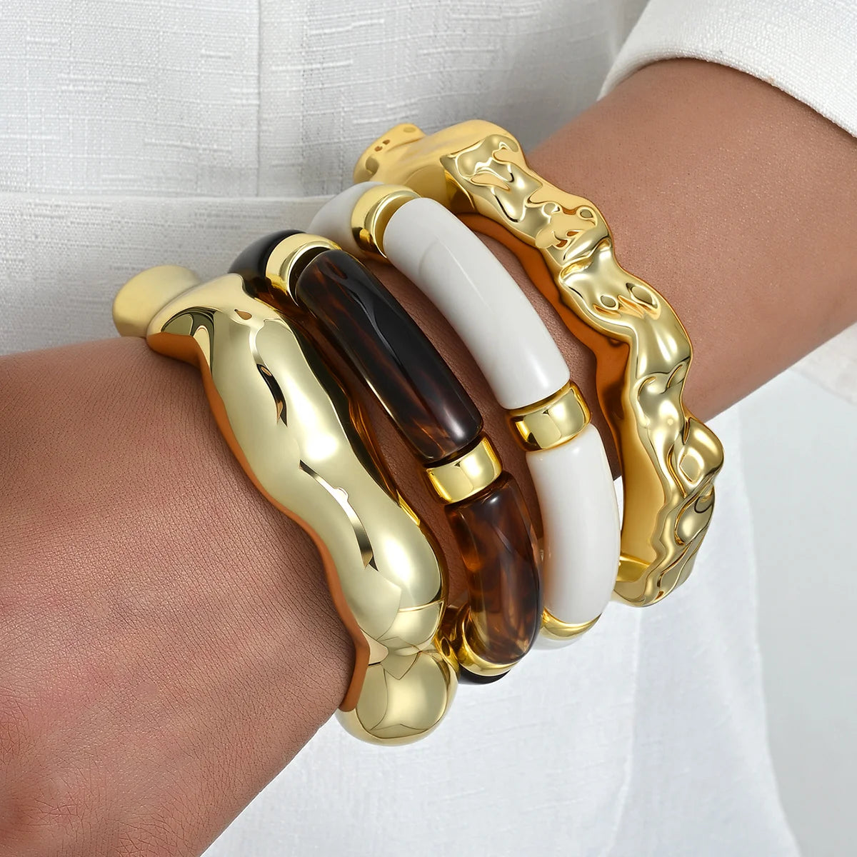 A set of vintage minimalist wavy bangle bracelets in gold and amber tones worn on a wrist.