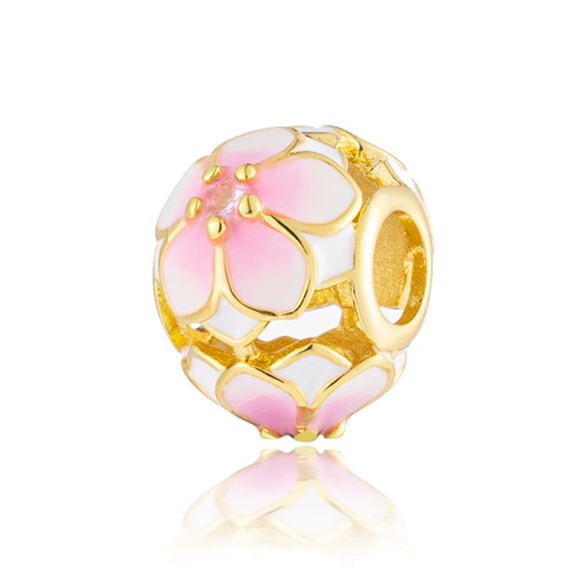 Un dije redondo con diseño floral rosa y blanco en chapado de oro.