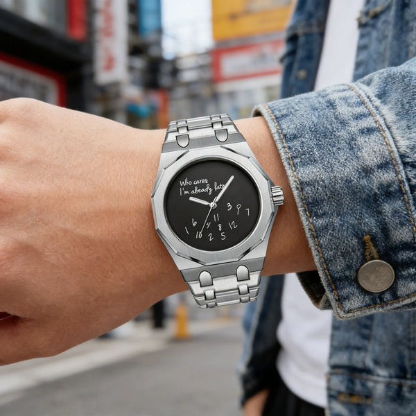 A close-up of a stainless steel watch with a black dial featuring the slogan Who cares I'm already late worn on a wrist.