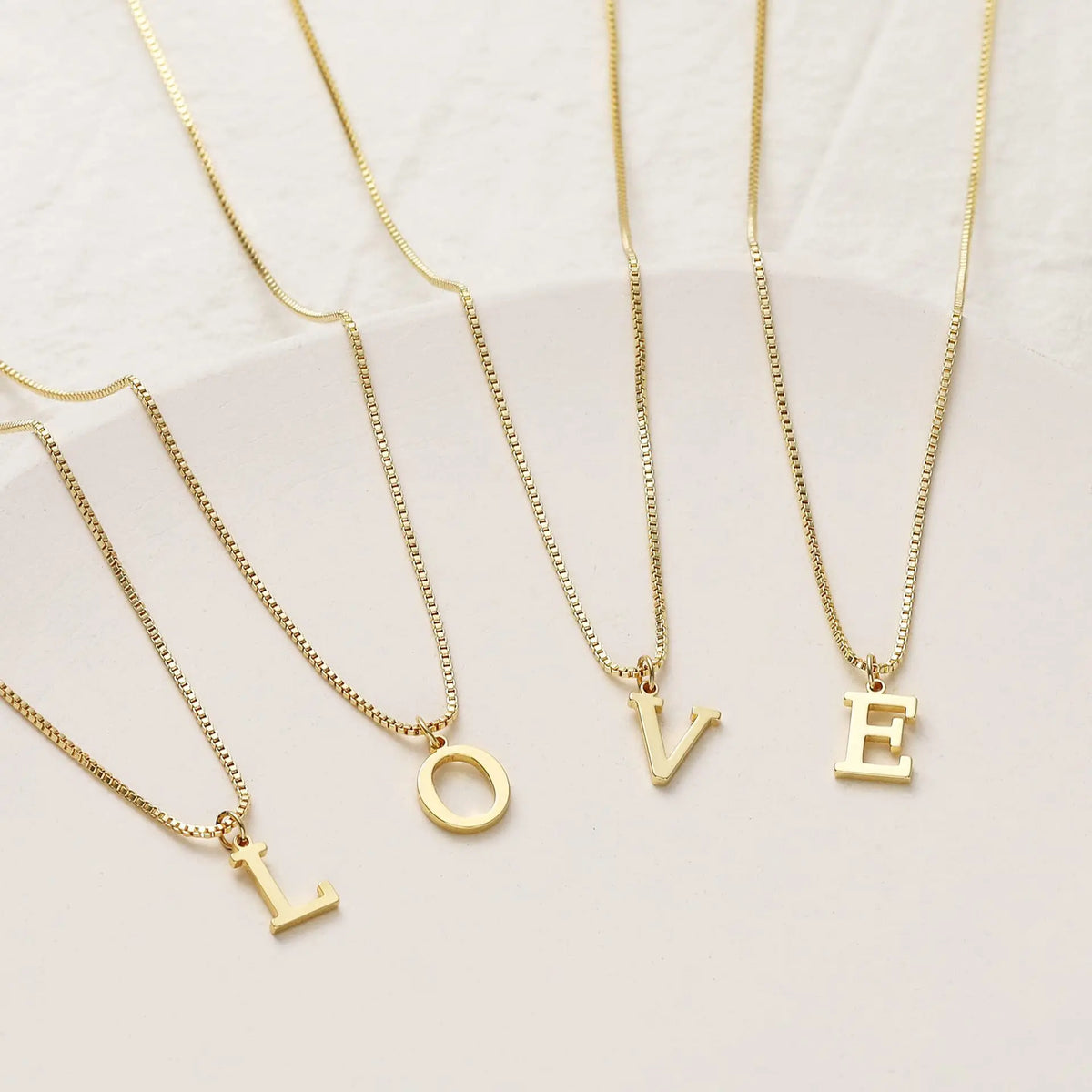 A set of delicate gold-plated initial letter necklaces featuring the letters O, L, V, and E.