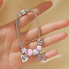 A silver beaded love bracelet set featuring various charms and pink stones worn on a hand.