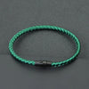 A green thread charm bracelet is displayed on a dark gray surface.