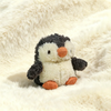 Un juguete de pingüino de peluche gris claro y blanco sobre una superficie blanca esponjosa.