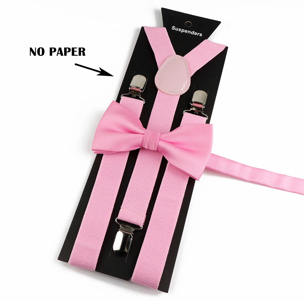 A set of pink polyester suspenders with bow ties and a pink button on a black background.