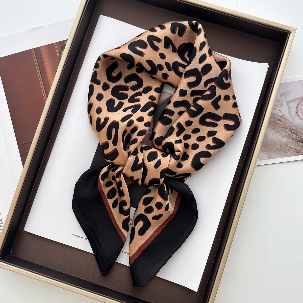 A luxury leopard print silk scarf tied in a bow, displayed in a brown box.