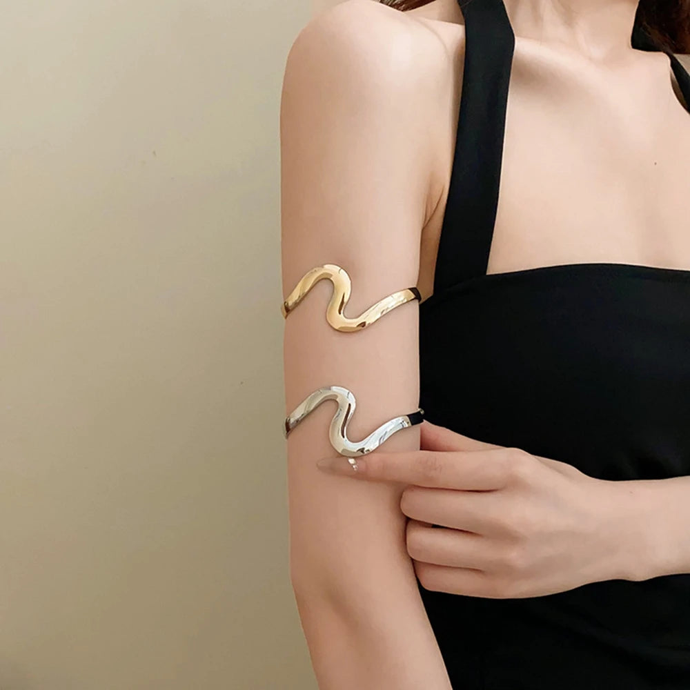 A close-up of a woman's arm showing two gold-plated swirl cuff bracelets on her wrist.