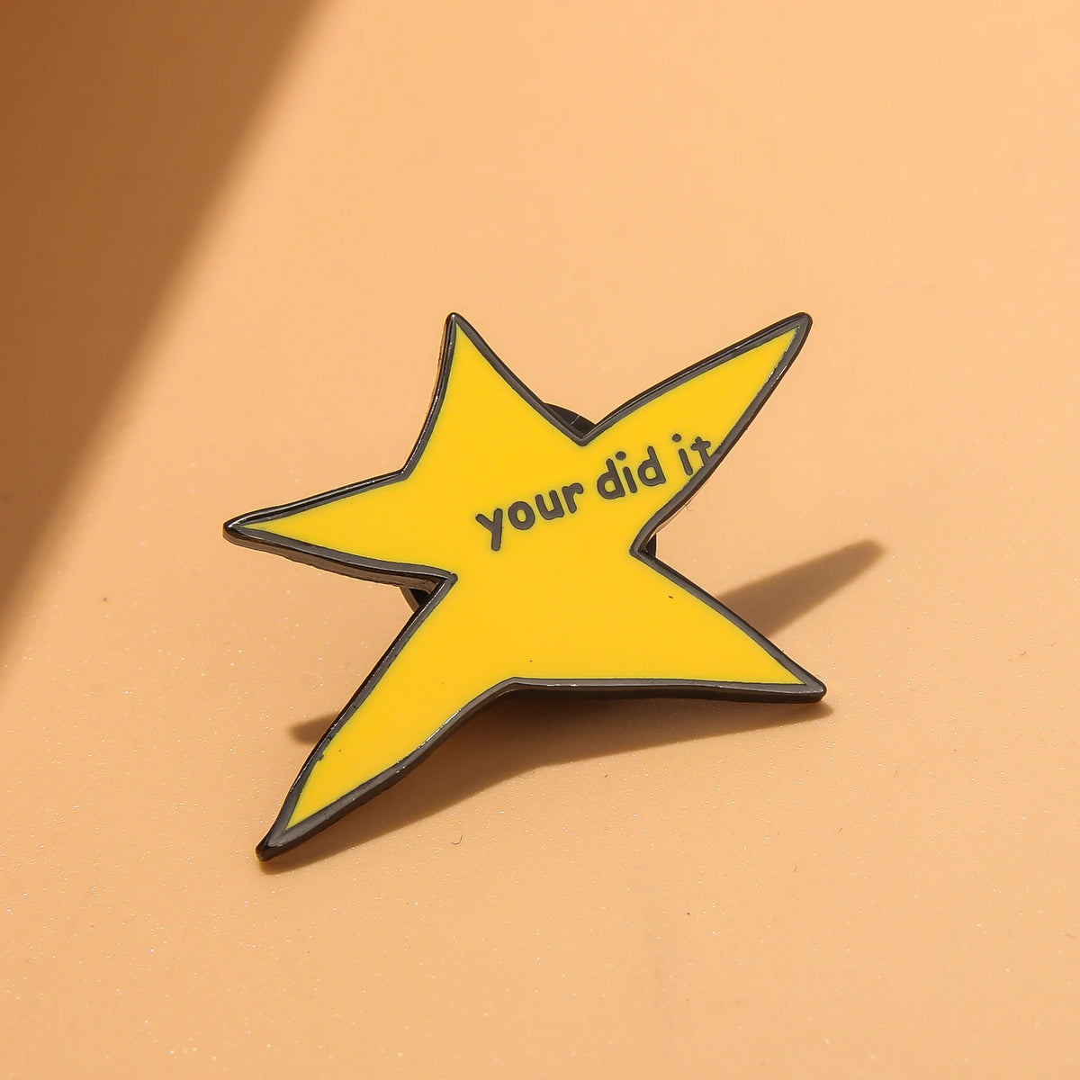 A yellow star-shaped enamel pin with the text you did it on a light orange background.